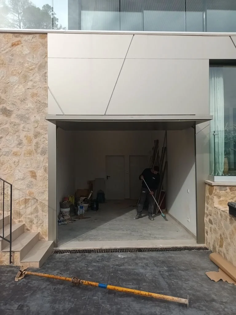 Un hombre trabajando en una entrada de garaje que está en construcción o remodelación, con herramientas y materiales en el interior.