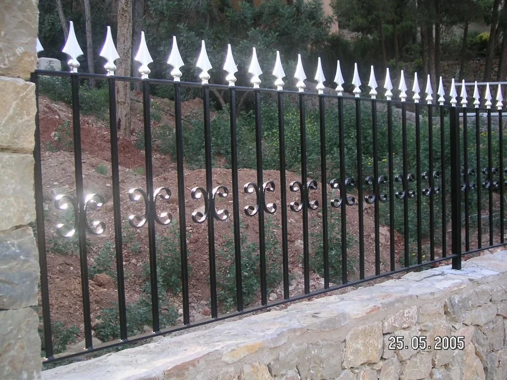Valla de hierro forjado con picos blancos decorativos sobre muro de piedra