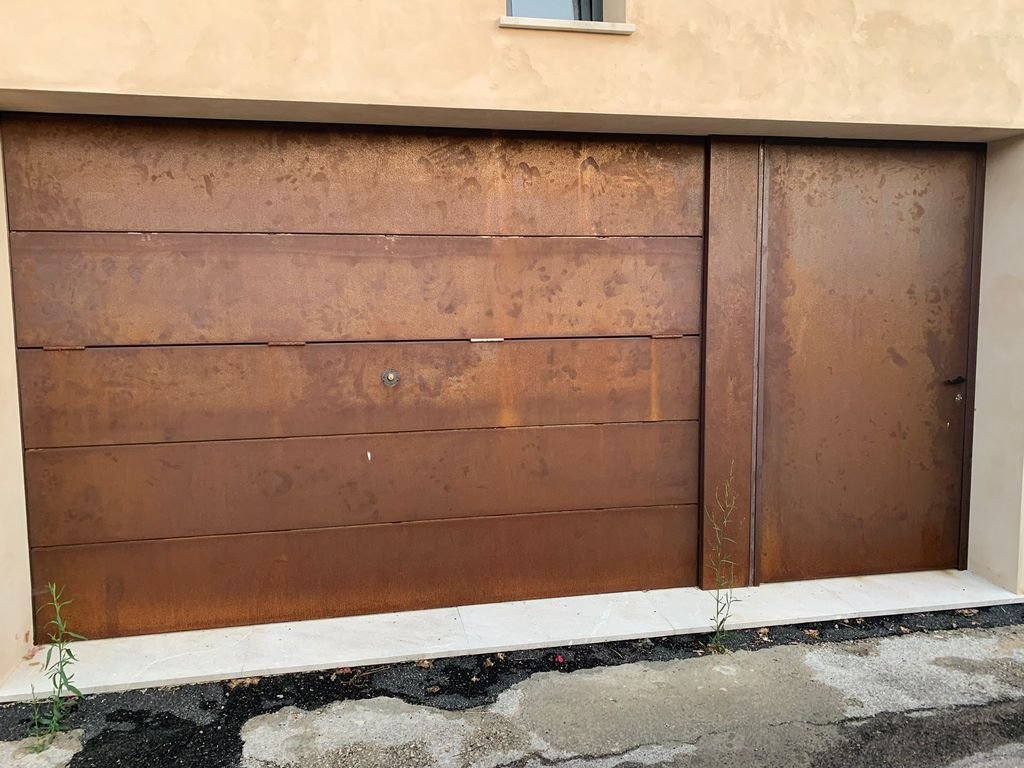 Puerta de garaje de metal oxidado en una casa, con algunos pequeños brotes de plantas en la base.