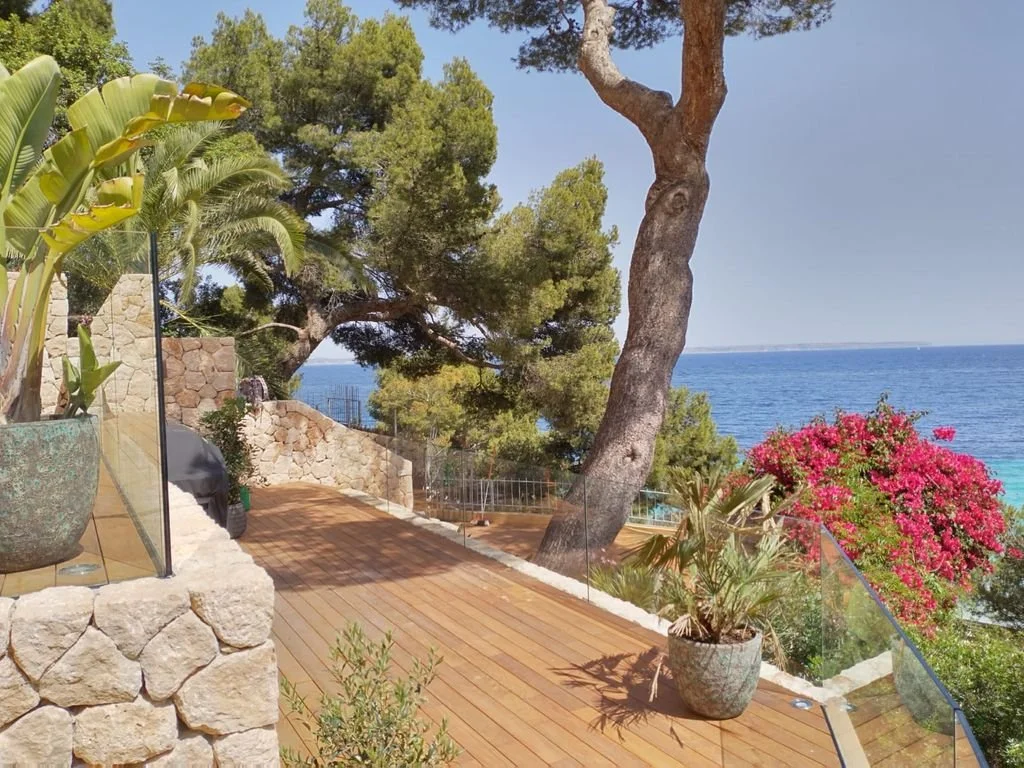 Vista de un balcón con plantas y vista al mar, árboles y flores coloridas