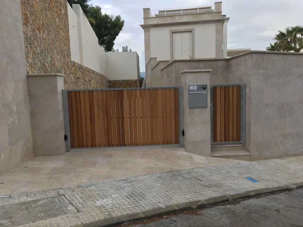 Puerta de entrada de madera con muro de piedra y pared de cemento, con buzón y caseta de intercomunicador, en una vivienda moderna.