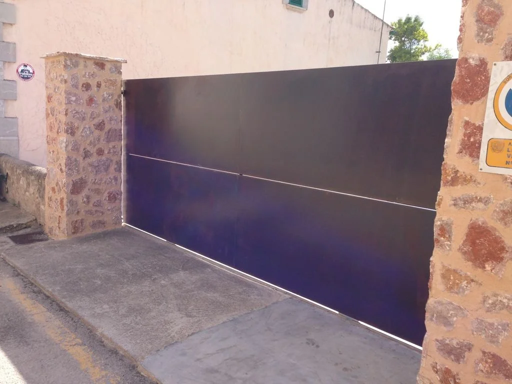 Puerta metálica de color azul en una entrada de muro de piedra en la calle.