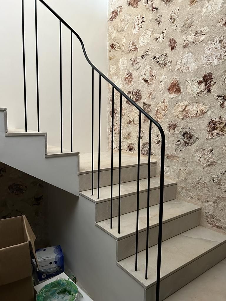 Escalera interior de mármol con barandal de metal negro, junto a pared de piedra rústica.