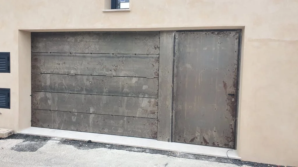 Puerta de garaje y puerta lateral de metal en un muro de concreto.