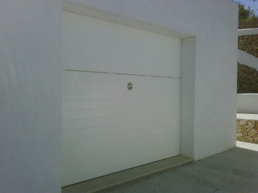 Puerta de garaje blanca en una pared blanca con un aspecto moderno y minimalista en un entorno exterior.