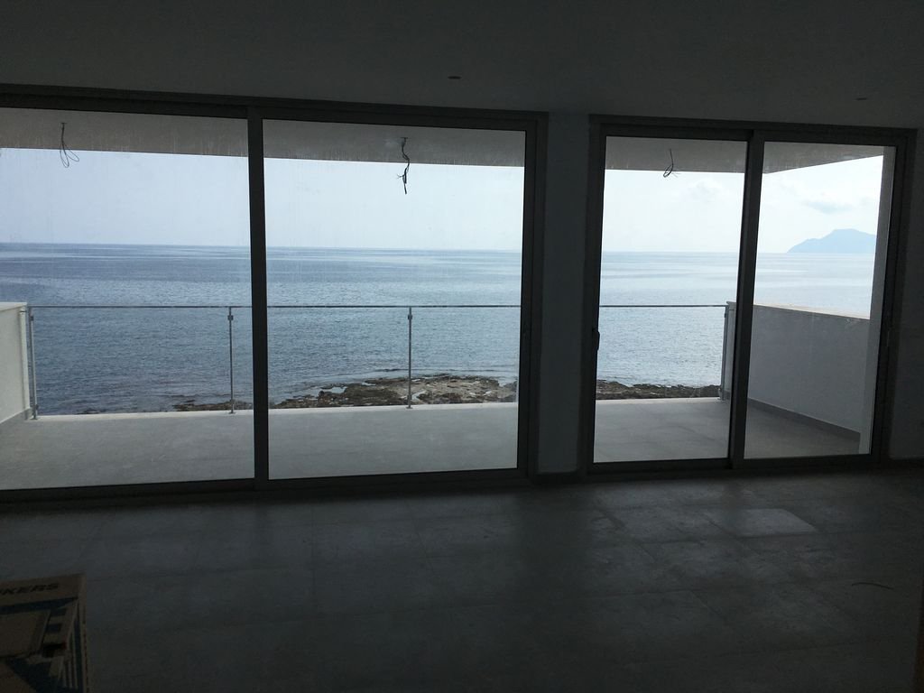 Vista del océano desde un balcón con puertas de cristal y barandilla, en un edificio en construcción.