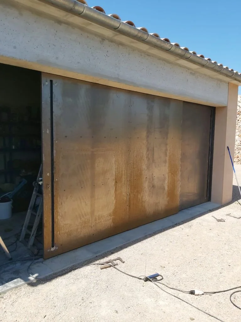 Puerta de garaje de acero con manchas de óxido y deterioro, en proceso de reparación en una cochera