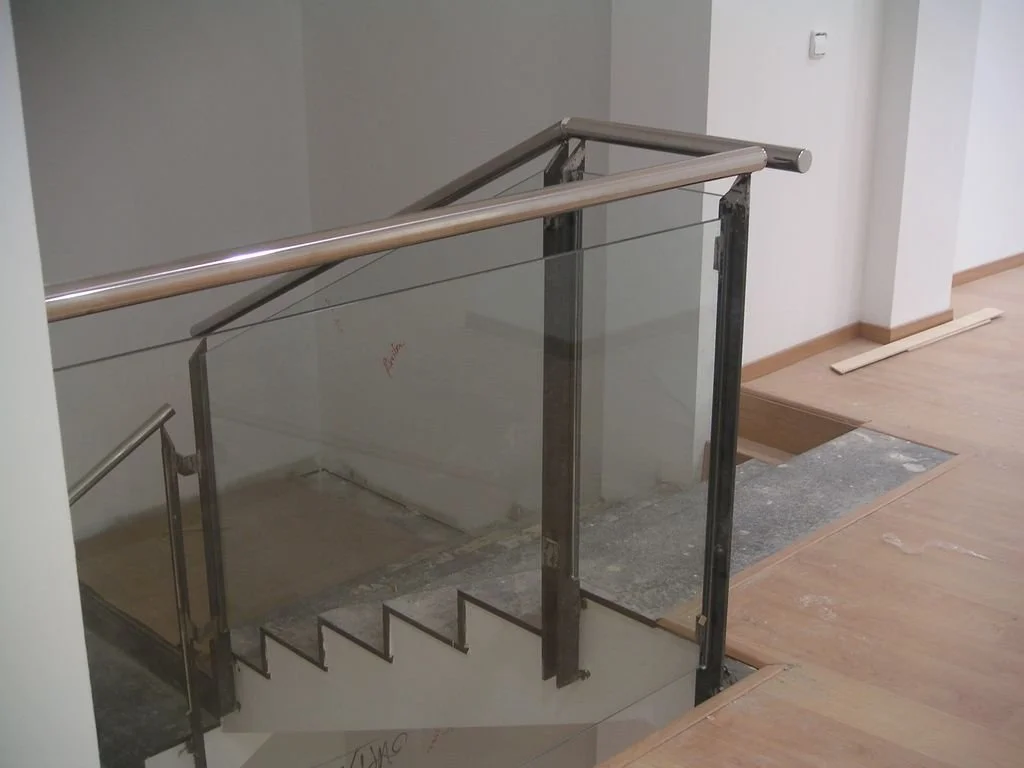 Escalera en construcción con barandal de metal y vidrio en un interior