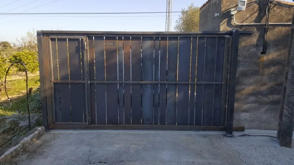 Puerta metálica negra instalada en una pared de cemento en un espacio exterior.