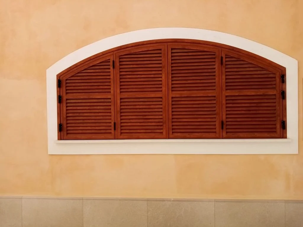 Ventana de madera con persianas enmarcada por una moldura blanca en una pared beige.
