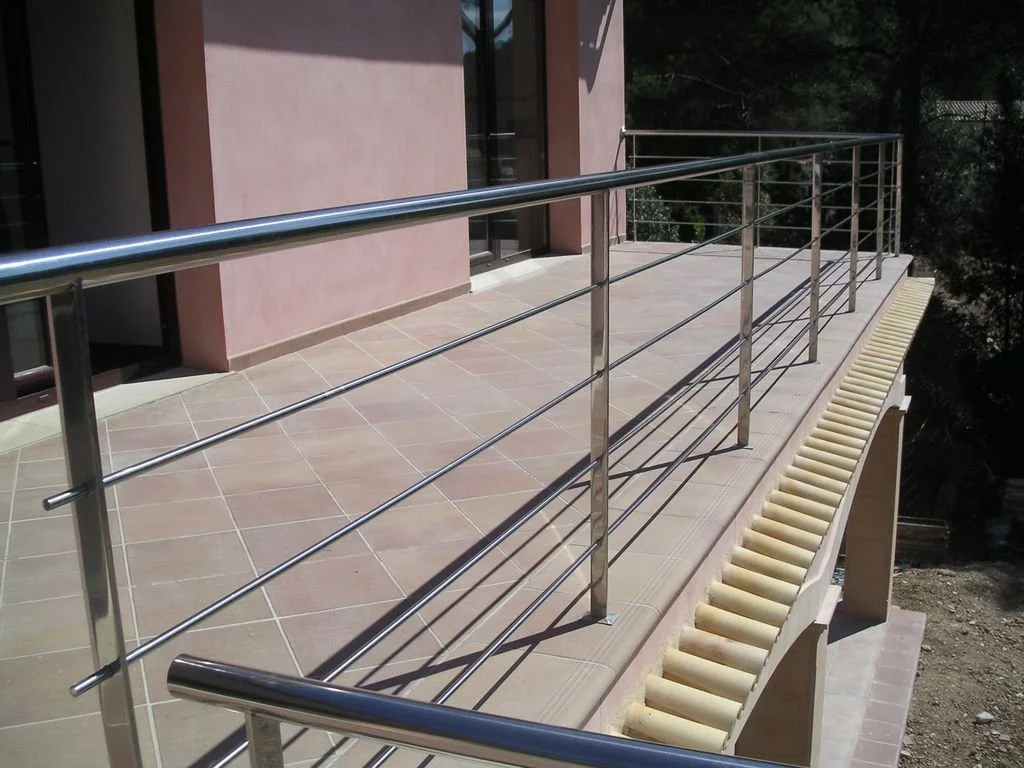Balustrada metálica en un balcón de edificio con vista hacia afuera y sombra en el suelo.