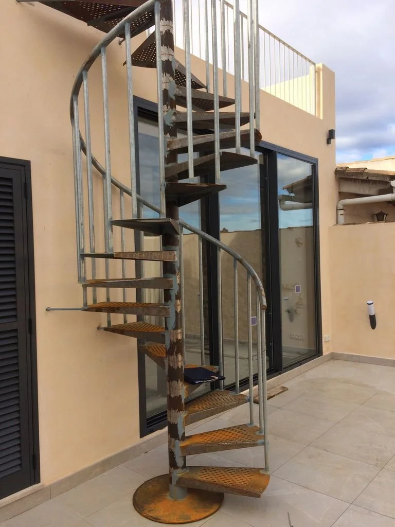 Escalera de caracol metálica en un balcón exterior de una casa.