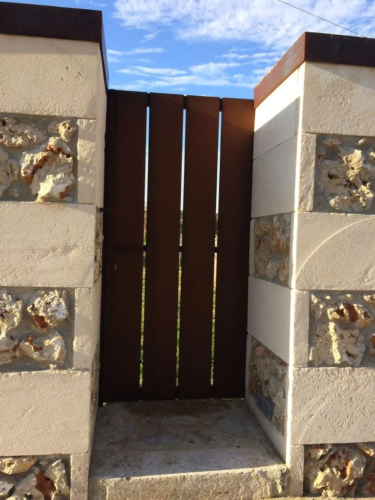 Puerta de madera entre columnas de piedra y yeso, con cielo azul y nubes al fondo.
