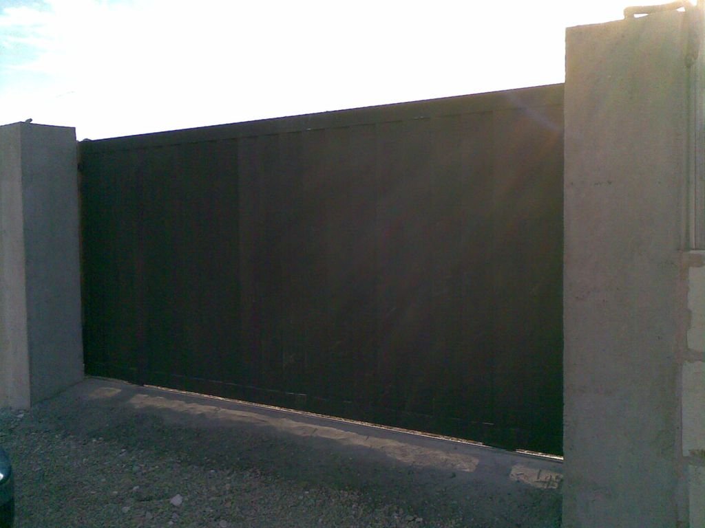 Puerta negra de metal en un muro de cemento, con costo de grava en el suelo.
