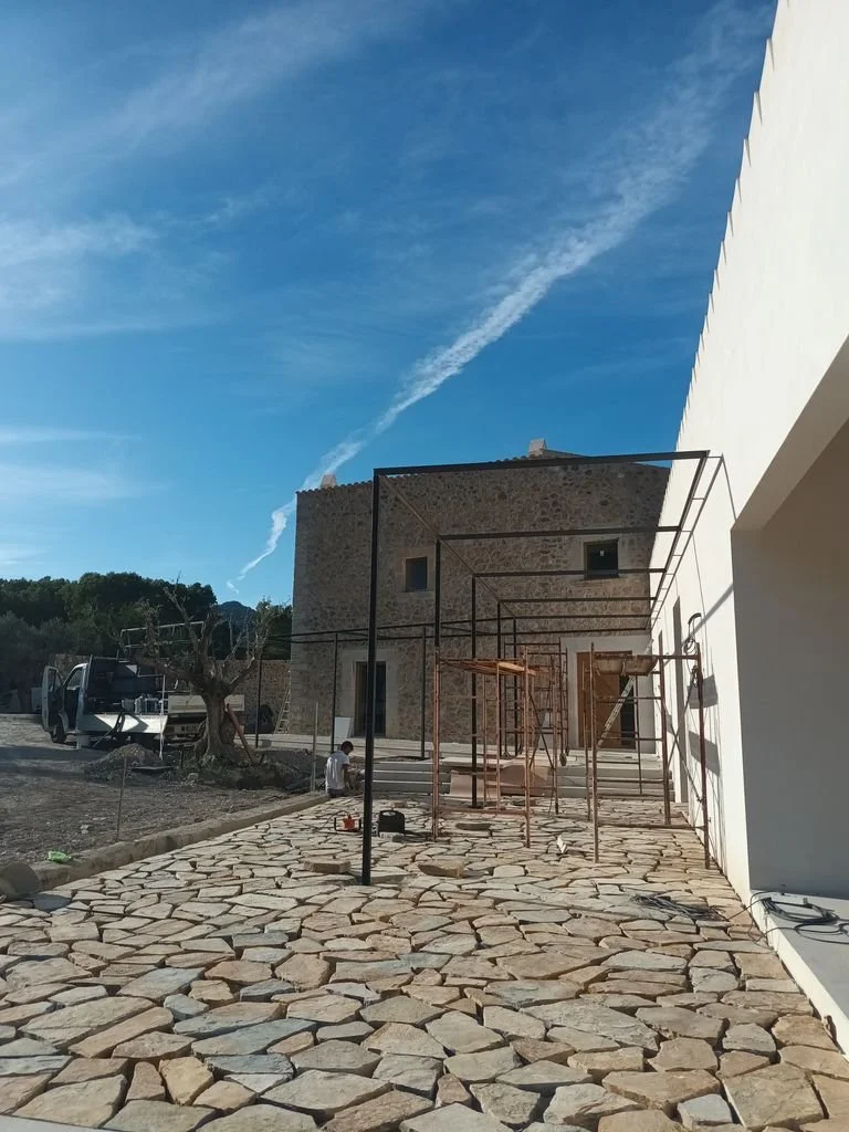 Construcción en progreso en una casa de piedra, con andamios y un cielo azul con nubes blancas.
