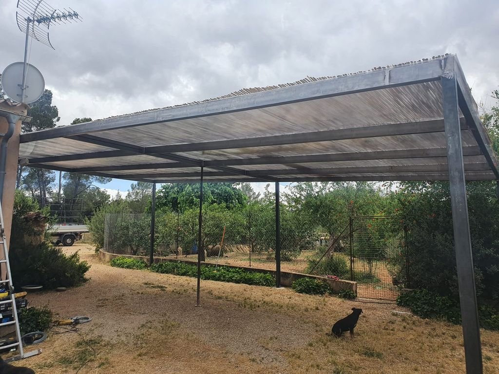 Estructura metálica con techado de lámina en un jardín con perros y árboles.