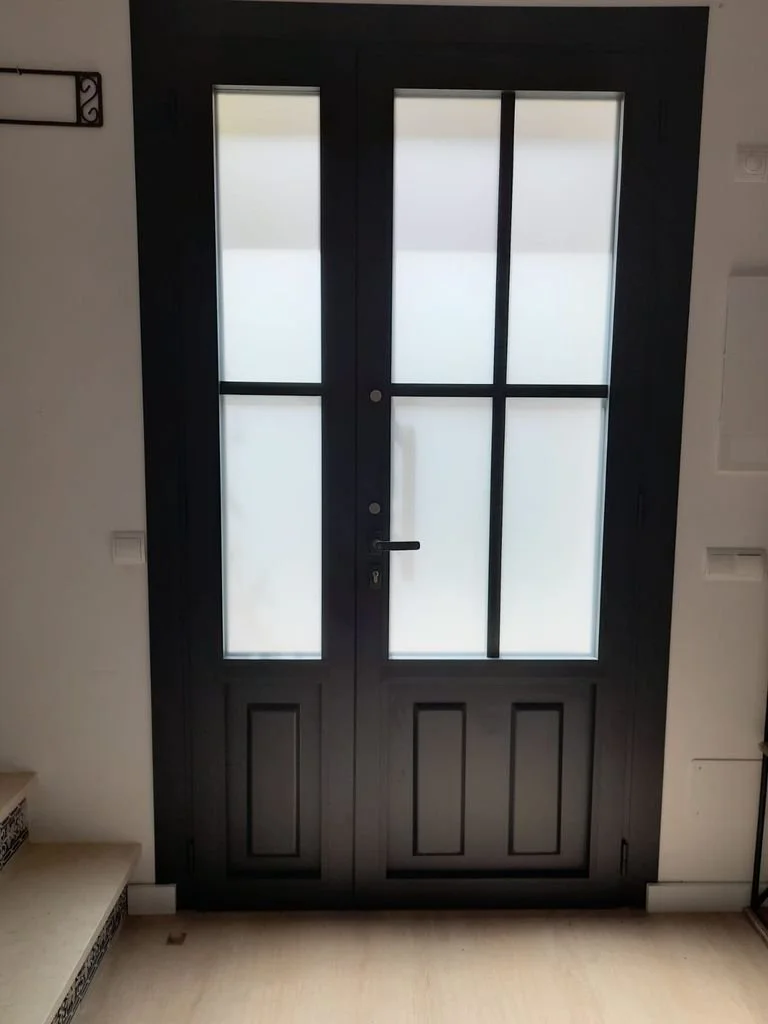 Puerta de madera negra con vidrio decorativo y marco delgado, ubicada en una pared interior.