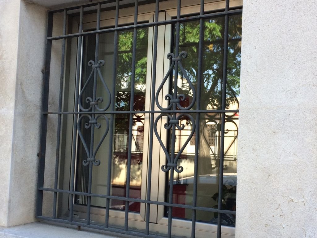 Ventana con reja de protección de hierro en un edificio, con reflejo del árbol y la calle en el vidrio