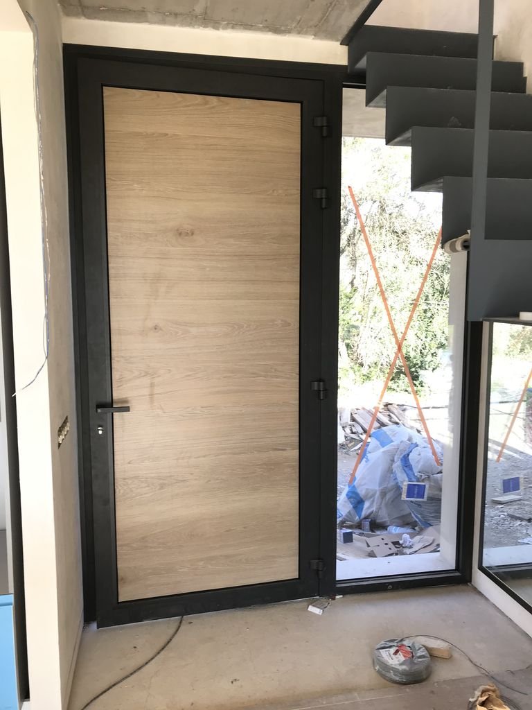 Puerta de madera y marco negro, con ventana grande a la derecha, en una ubicación en construcción o renovación.