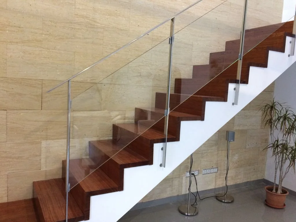 Escalera moderna con peldaños de madera y barandilla de cristal en un espacio interior, con pared de textura beige y planta en maceta a la derecha.