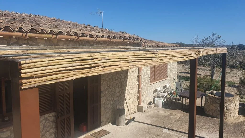 Casa de piedra con terraza cubierta de cañas de bambú y muebles al aire libre