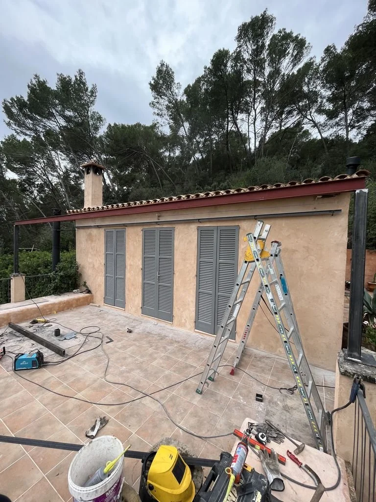 Reconstrucción de una pared con persianas charol en un balcón, en un ambiente con herramientas de construcción y unas escaleras.