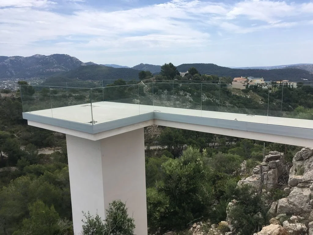 Una terraza moderna con barandilla de cristal en un paisaje montañoso y vegetación.