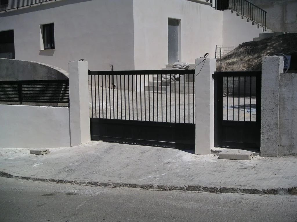 Puerta de hierro negro con poste de concreto, y muro de muro y patio de construcción en una casa de varios pisos.