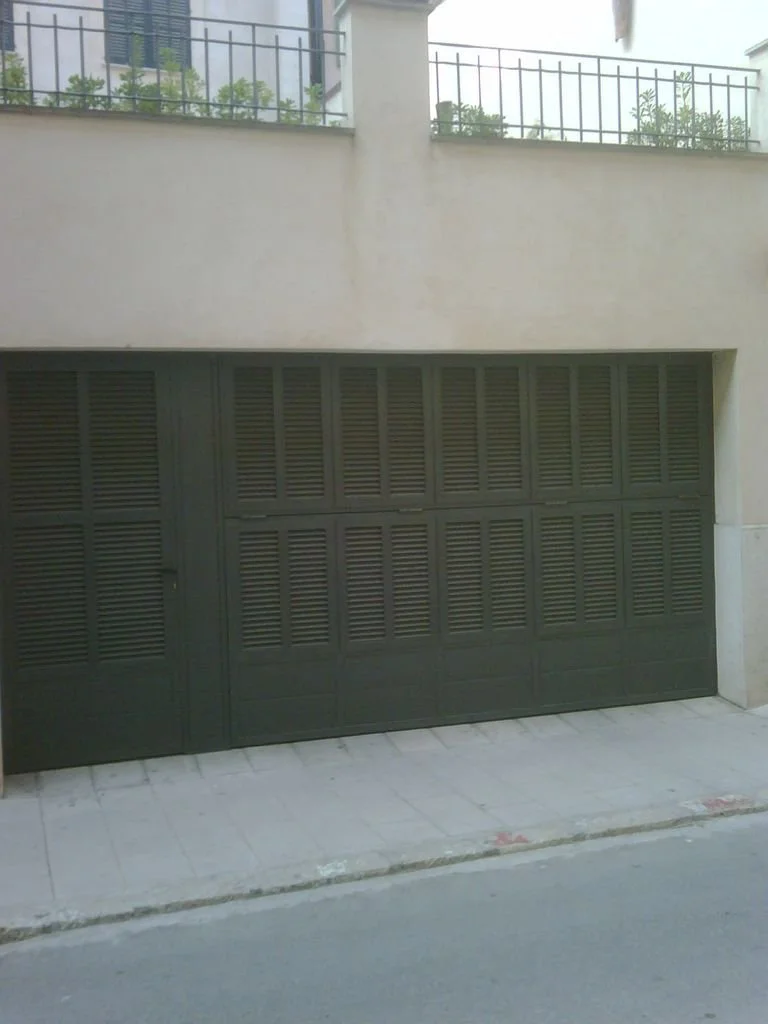 Puerta de garaje de color oscuro con persianas horizontales, ubicada en una fachada de edificio moderno.