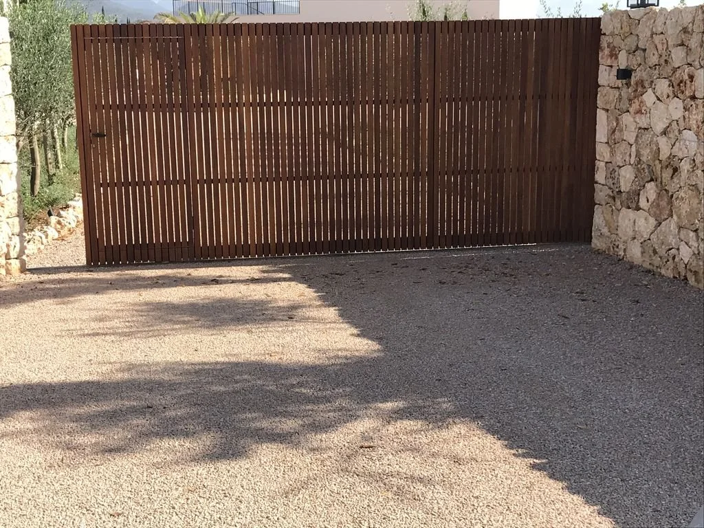 Una puerta de madera en un muro de piedra, delimitando un espacio exterior con suelo de grava.