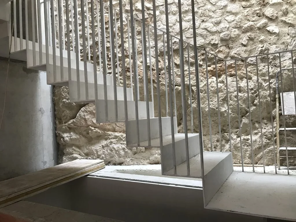 Escalera de concreto con barandillas de metal, construida en un espacio con paredes de piedra y un fondo que muestra una pared de piedra rugosa.
