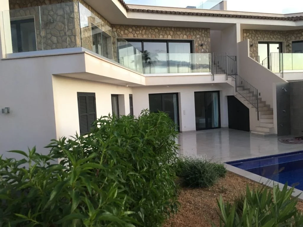 Casa moderna con balcón de vidrio, escaleras exteriores y piscina, vista desde el jardín.