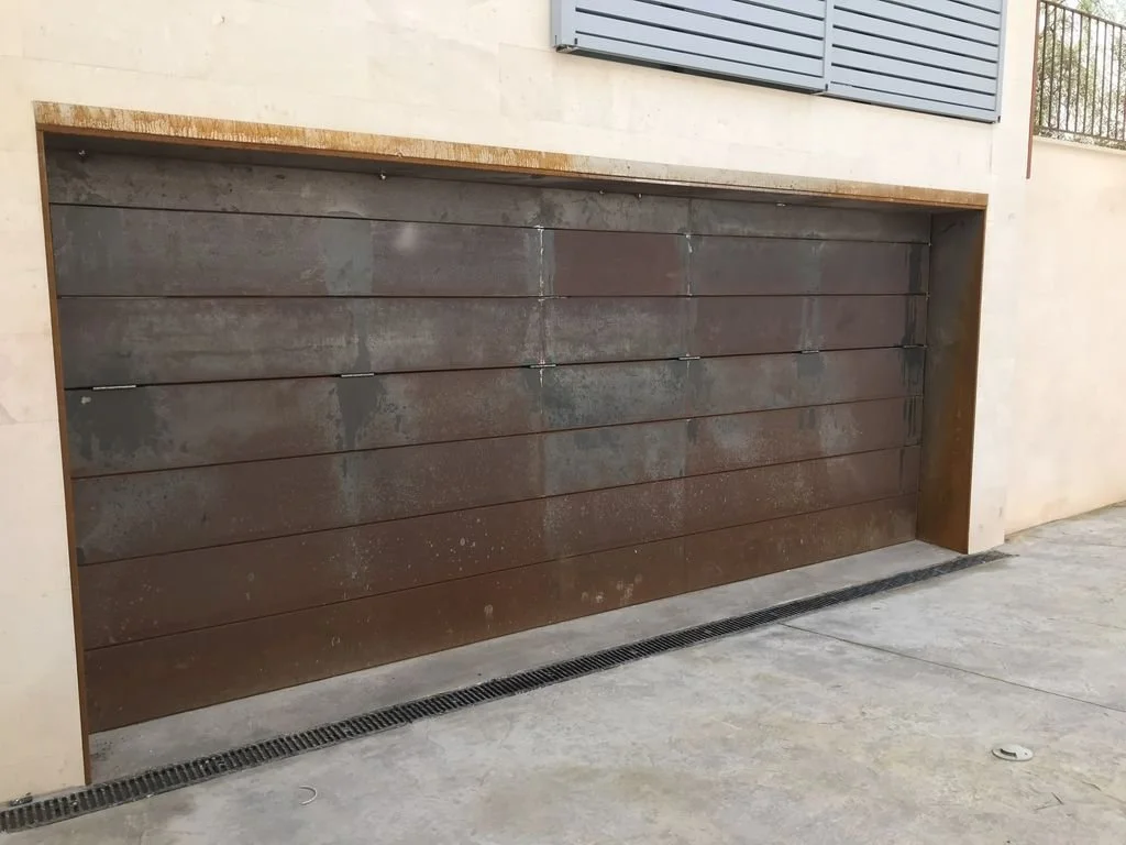 Puerta de garaje metálica oscura con manchas de óxido en un edificio