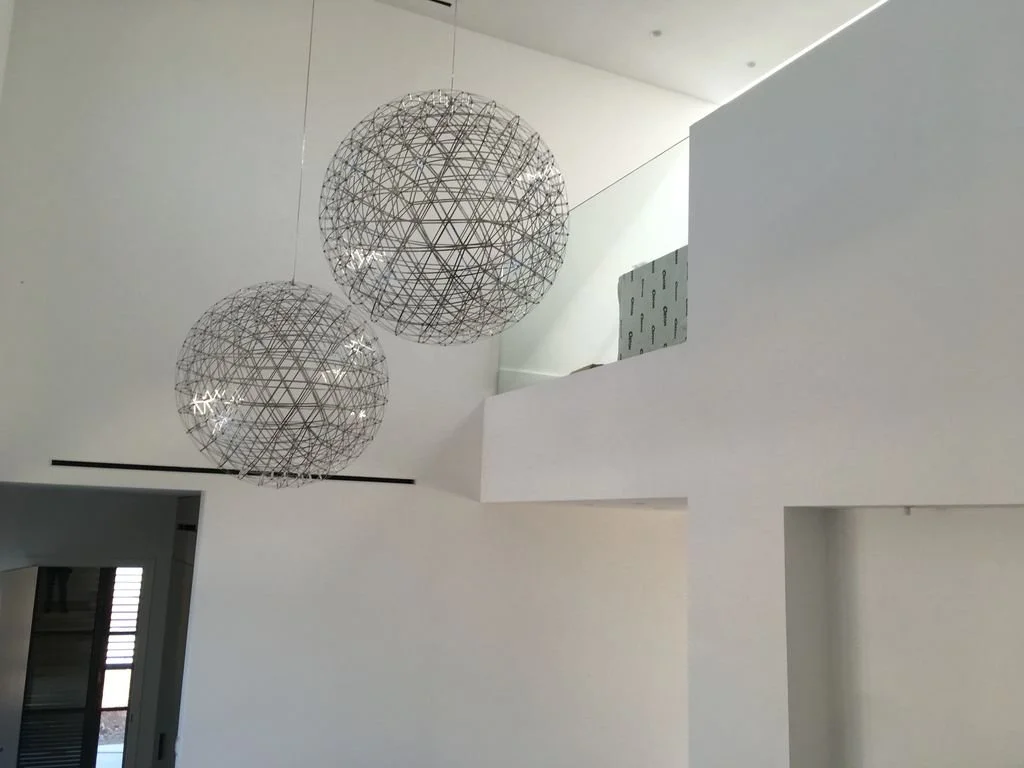 Dos lámparas de diseño moderno colgando del techo en un espacio blanco y minimalista.