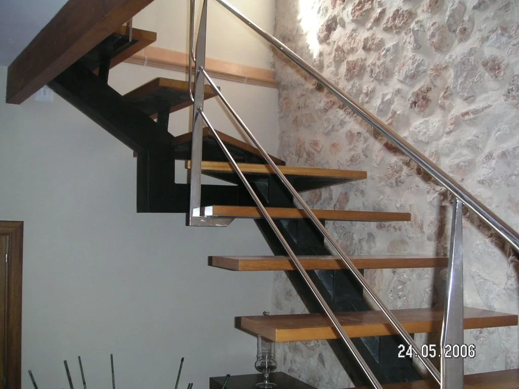 Escalera moderna de metal y madera en interior con pared de piedra antigua.