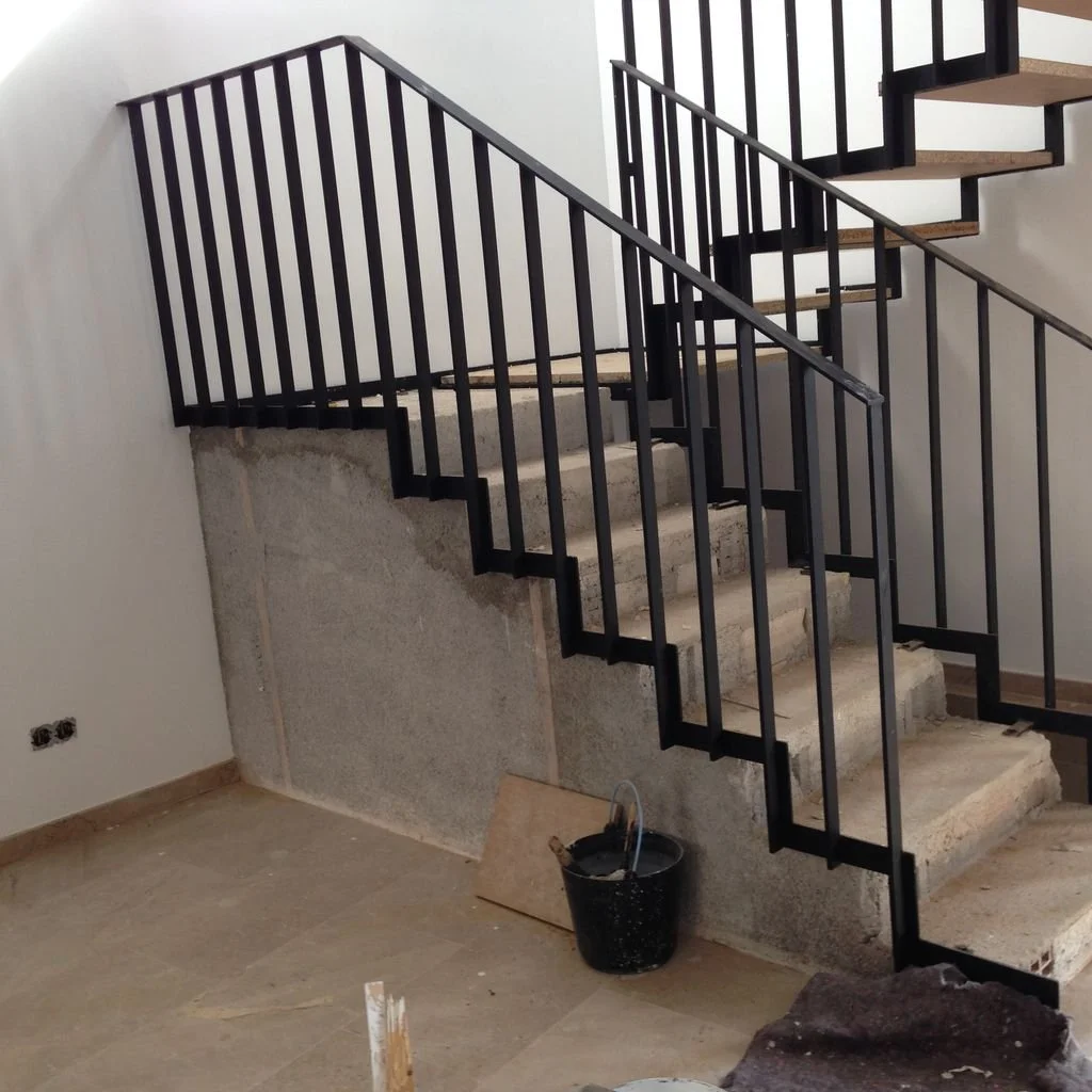 Escalera de concreto en construcción con barandilla negra instalada parcialmente en un edificio en construcción.