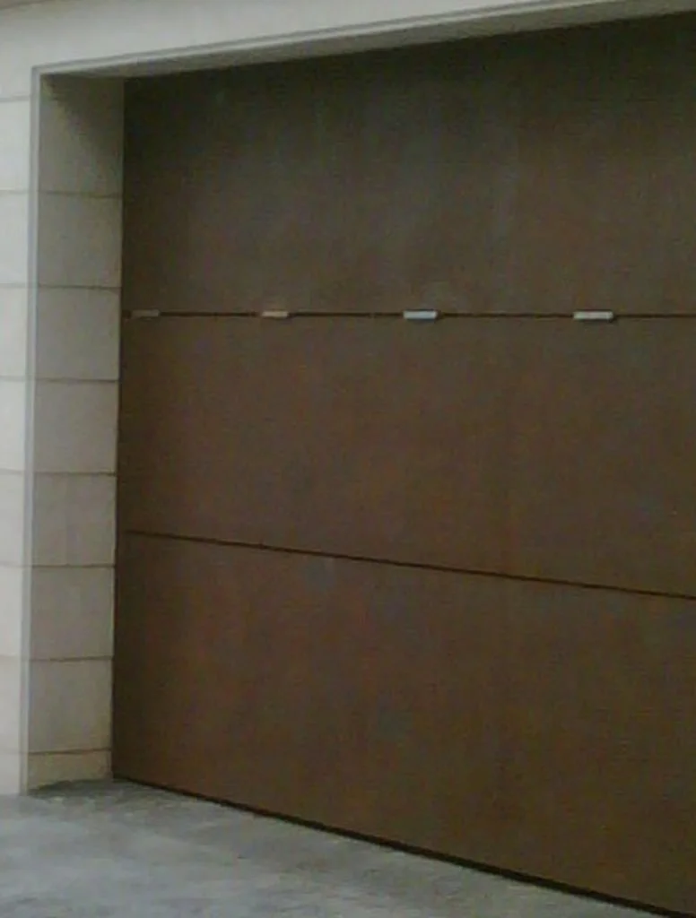 Puerta de garaje automática de color marrón en una pared de piedra beige.