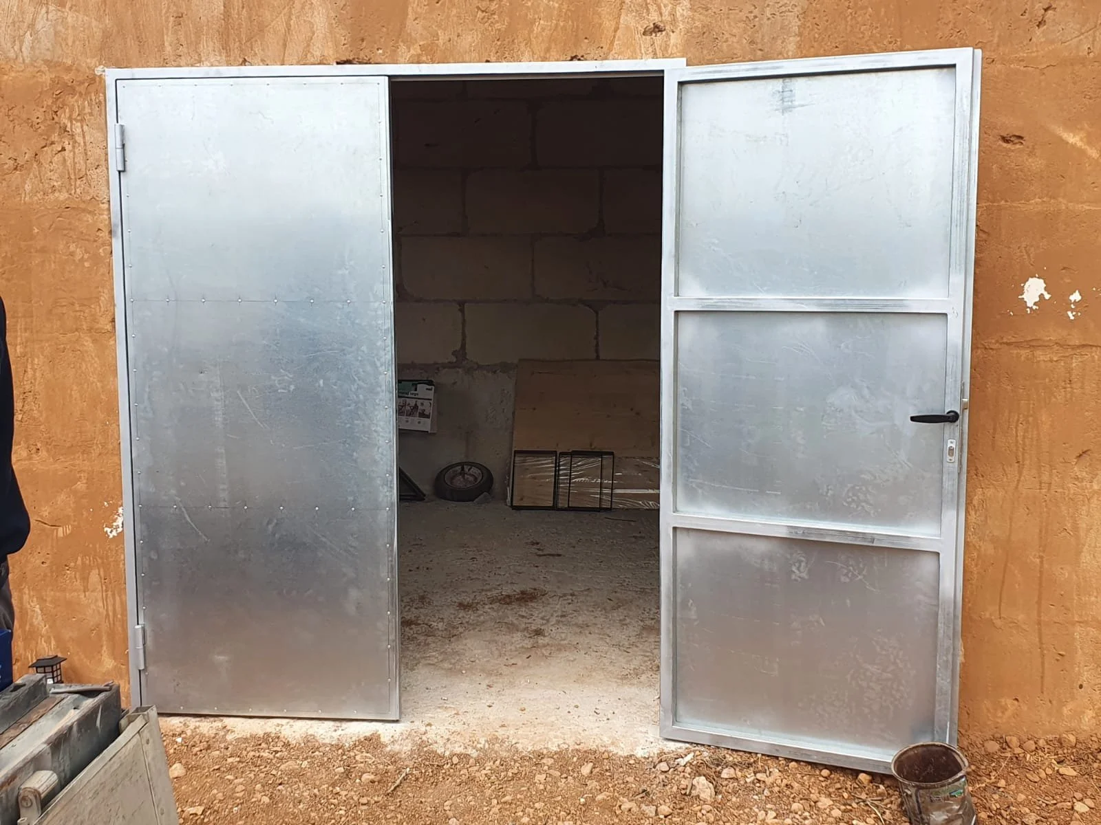 Puerta de metal de doble hoja que da acceso a un interior con paredes de bloques de cemento, en construcción o reparación.