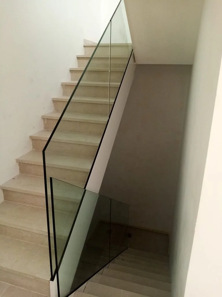 Escalera interior con barandal de vidrio y bordes negros.