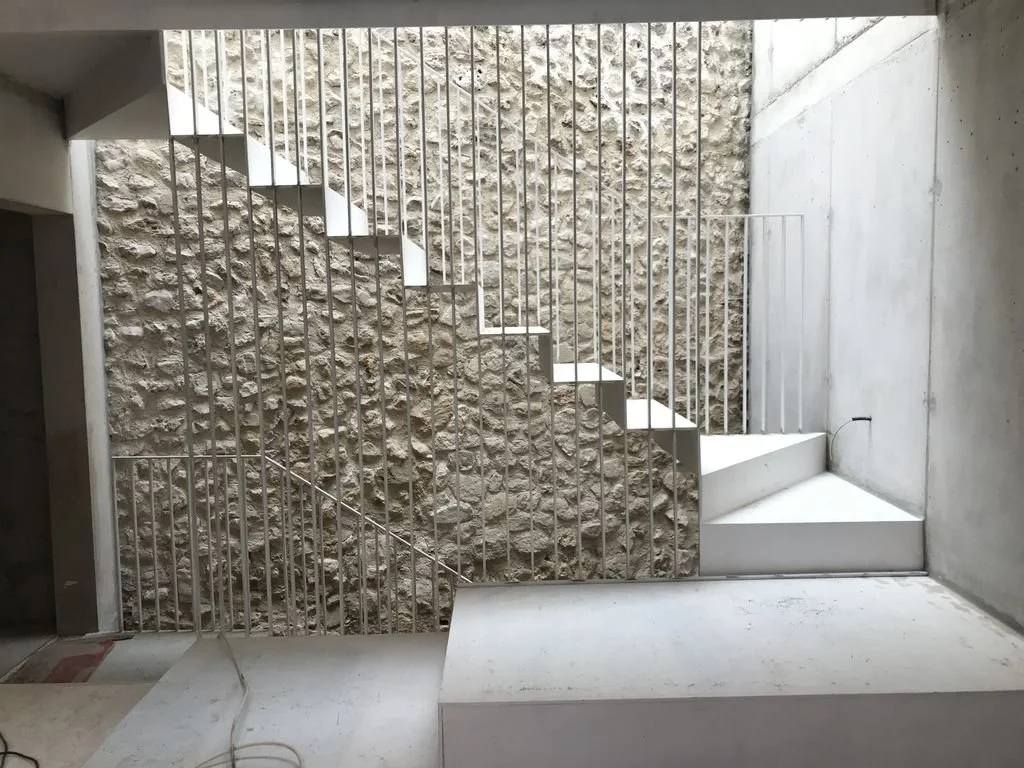 Escalera moderna en un espacio interior con paredes de piedra y concreto.