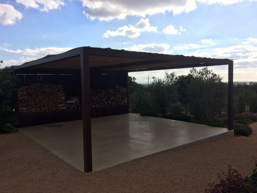 Estructura cubierta con leña apilada, en un espacio abierto con vista a la naturaleza y cielo con nubes.