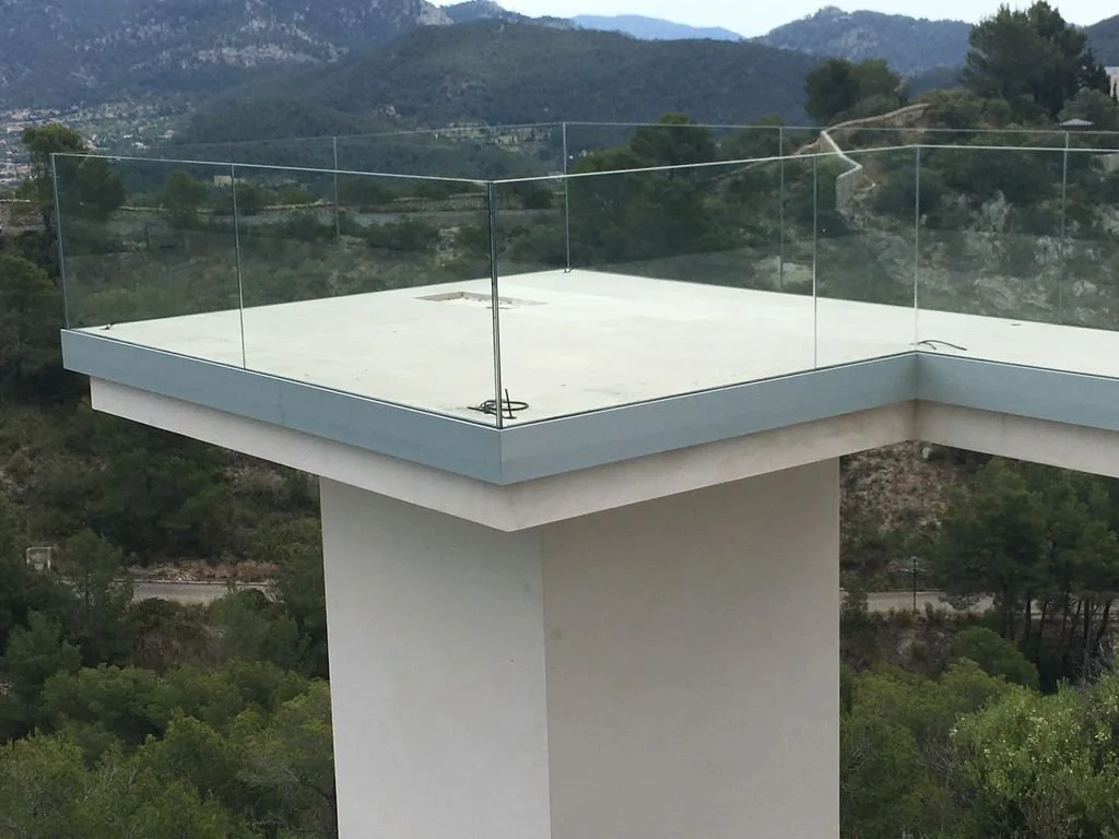 Terraza moderna con barandal de vidrio en la cima de una estructura, rodeada de árboles y montañas.