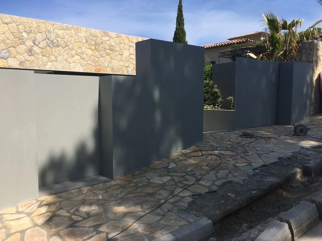 Muros de concreto gris en construcción en un patio con suelo de piedra, con herramientas eléctricas y cables en el suelo.