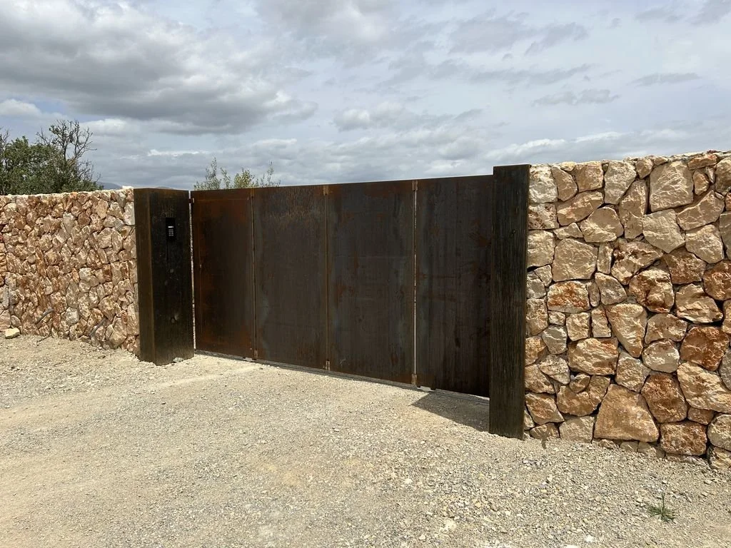 Puerta de metal en un muro de piedras, en un entorno exterior con cielo nublado.