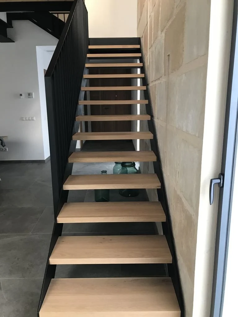 Escalera moderna de madera y metal en interior de casa con pared de piedra y ventanales.