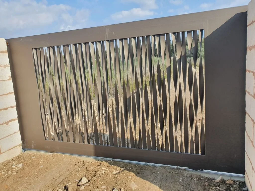 Cancelación de hierro con diseño decorativo en forma de ondas, colocada en una entrada de muro de ladrillos, en un área exterior con suelo de tierra.