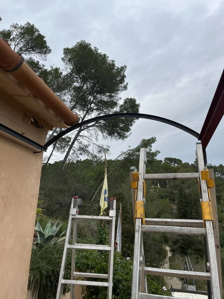 Escaleras de aluminio frente a una casa, con árboles y cielo nublado de fondo.