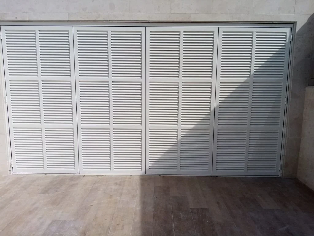 Puerta de persiana blanca con listones horizontales en un muro de piedra.