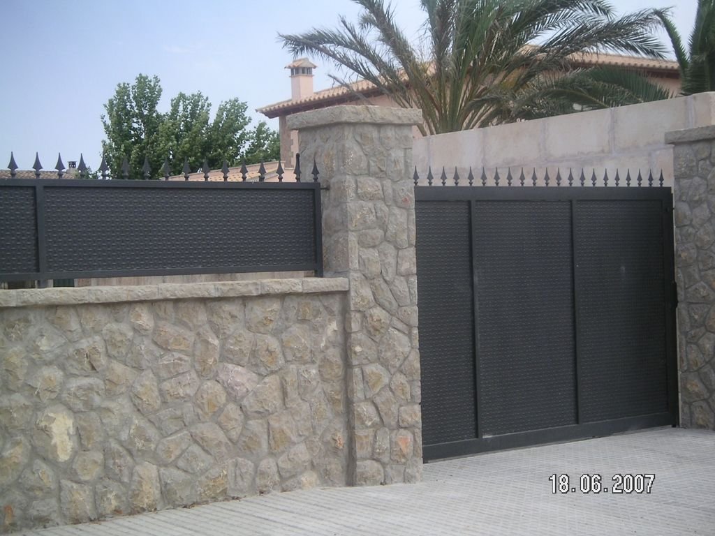 Entrada de una casa con muro de piedra y puerta y reja de metal negro.