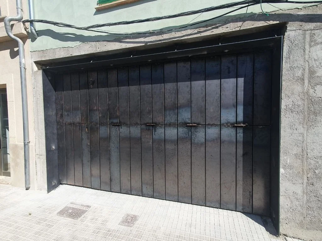 Puerta metálica negra de garaje en una pared de concreto.